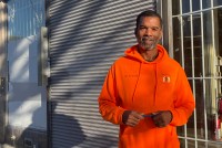 A photo of a man in a bright orange hoodie standing outside.