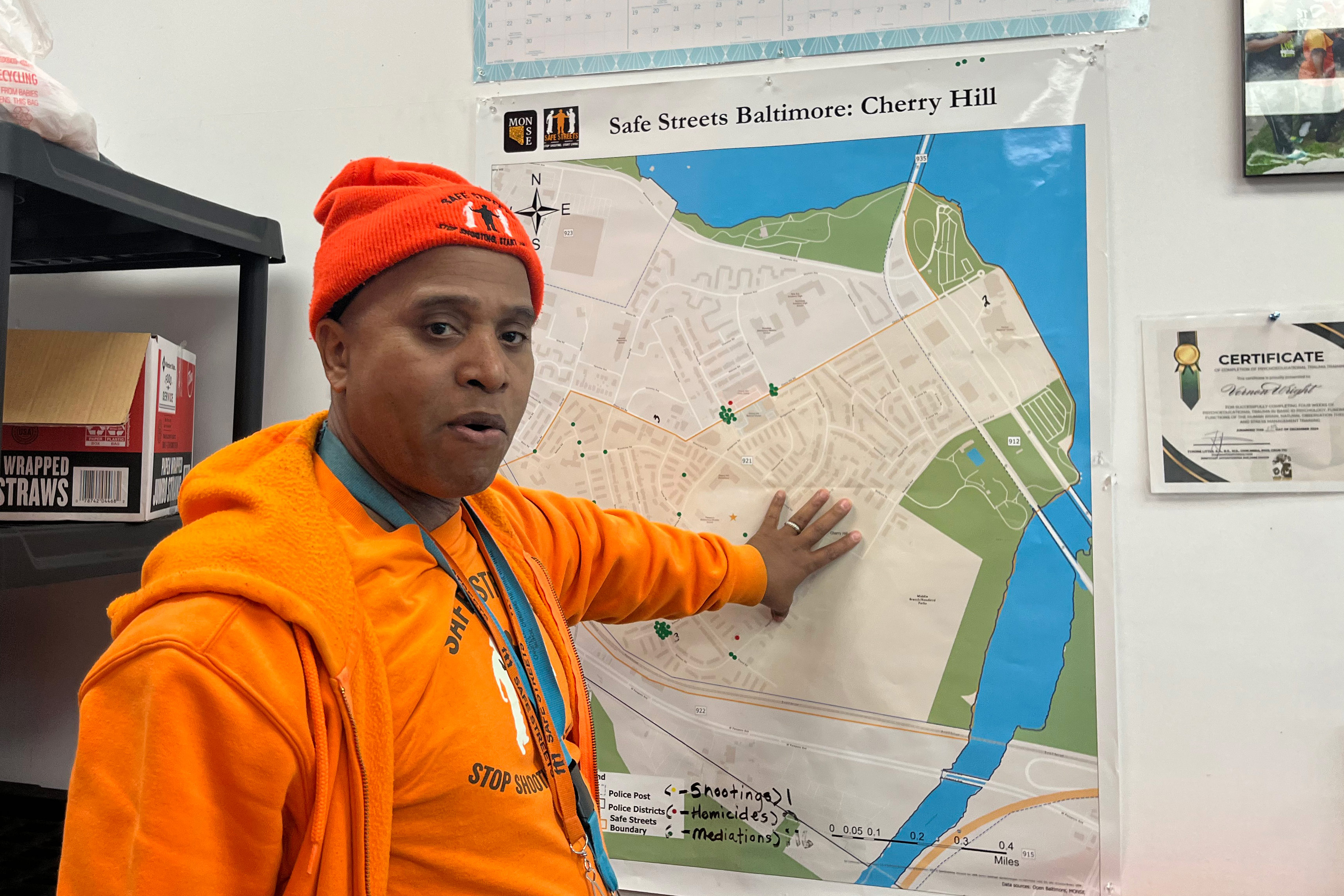 A photo of a Safe Streets worker in bright orange. He points to a map of Baltimore.