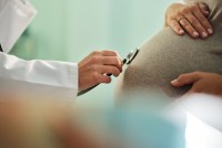 A close up of photograph of an unrecognizable doctor using stethoscope while listening to the belly of a pregnant woman.