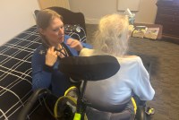 A photo of a nurse practitioner examining an older woman patient in her home.
